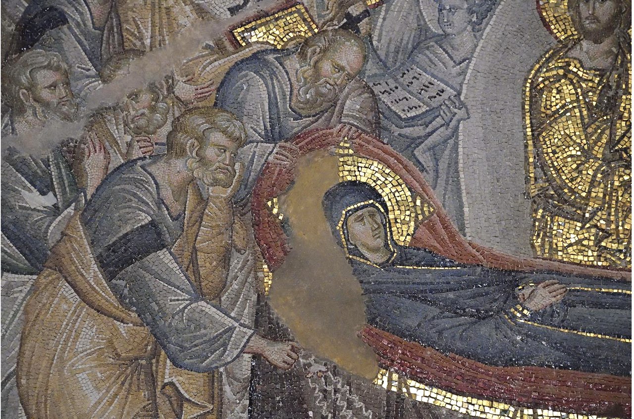 Detailed section of a Byzantine mosaic depicting a solemn religious scene with several figures, including a central figure of the Virgin Mary in dark robes, surrounded by saints and apostles with halos and ancient script, all set against a gold background