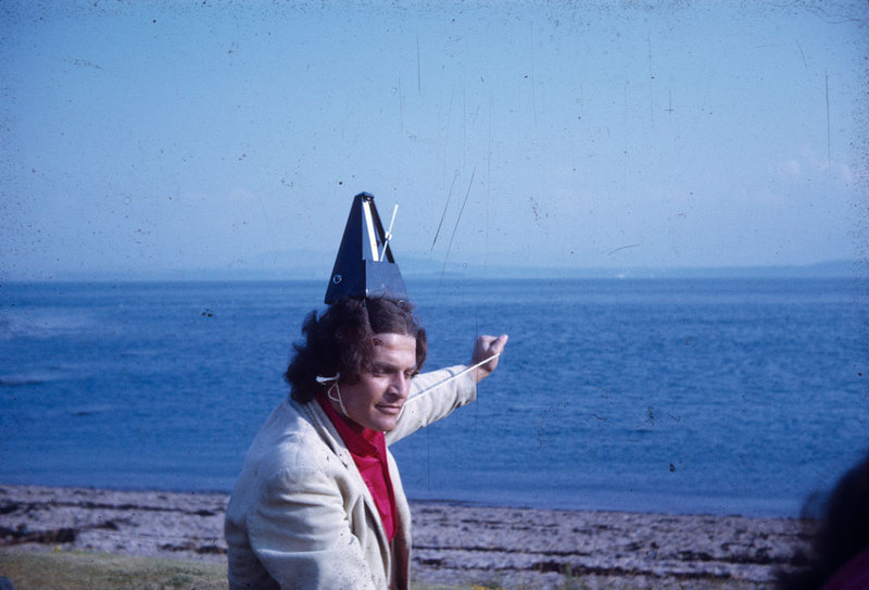 Photograph of a man wearing a metronome on top of his head with sea in the background